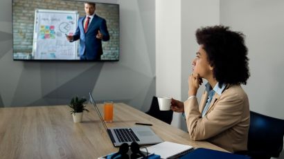 Businesswoman listening to an online business seminar via a video conference screen in an office.