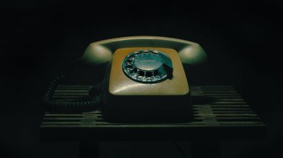 Vintage rotary dial telephone resting on a slatted wooden table against a dark background.