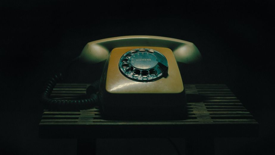 Vintage rotary dial telephone resting on a slatted wooden table against a dark background.