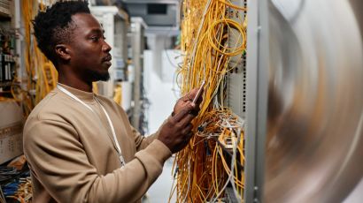 System administrator checking server rack cables with a smartphone in a data centre.