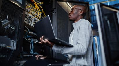 An engineer holding a laptop while managing network servers and cabling in a data centre.