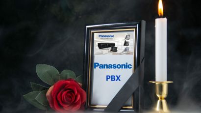 Framed photo of Panasonic PBX with a mourning ribbon, beside a lit candle and a red rose.