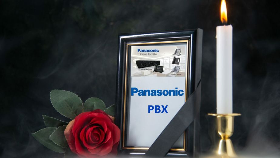 Framed photo of Panasonic PBX with a mourning ribbon, beside a lit candle and a red rose.